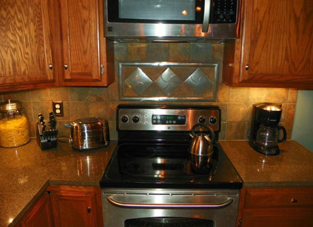 Cette photo montre une cuisine chic en U et bois brun de taille moyenne avec une crédence orange, un électroménager en acier inoxydable, un sol en carrelage de céramique et une péninsule.