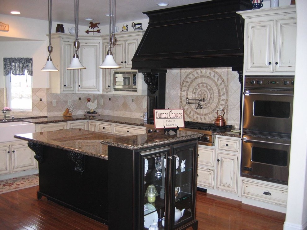 Inspiration for a large timeless u-shaped medium tone wood floor kitchen remodel in Sacramento with a farmhouse sink, raised-panel cabinets, distressed cabinets, granite countertops, beige backsplash, terra-cotta backsplash, stainless steel appliances and an island
