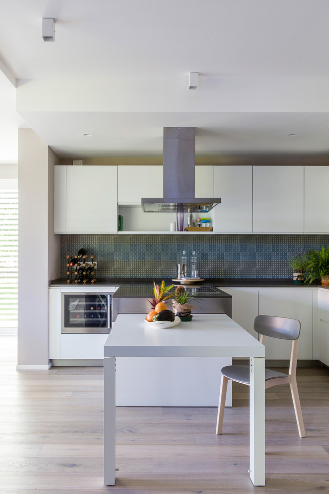 Idéer för ett mellanstort modernt grå kök, med släta luckor, vita skåp, blått stänkskydd, ljust trägolv, en halv köksö, beiget golv, en undermonterad diskho och rostfria vitvaror