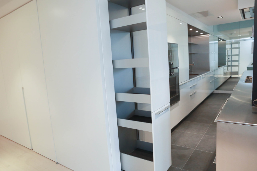 This is an example of an expansive modern galley kitchen in Los Angeles with a submerged sink, flat-panel cabinets, white cabinets, stainless steel worktops, metallic splashback, stainless steel appliances, porcelain flooring, multiple islands and grey floors.