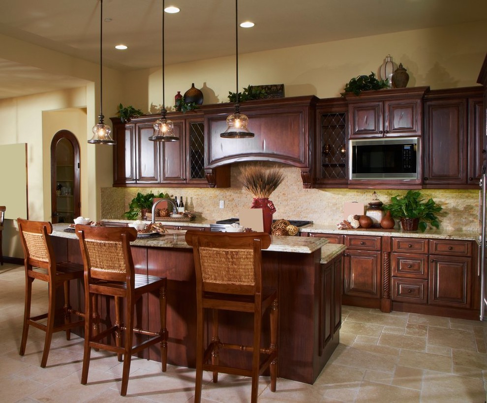 Open concept kitchen - mid-sized tropical l-shaped limestone floor and beige floor open concept kitchen idea in San Francisco with raised-panel cabinets, dark wood cabinets, granite countertops, beige backsplash, stone tile backsplash, stainless steel appliances and an island