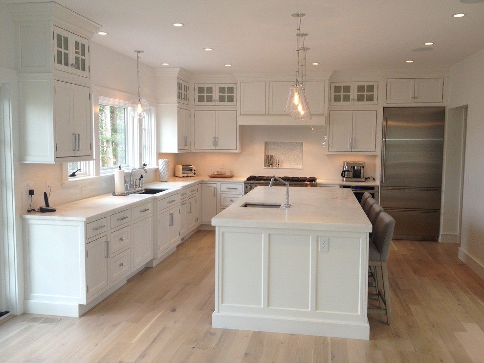 This is an example of a large contemporary l-shaped kitchen/diner in Boston with a single-bowl sink, shaker cabinets, white cabinets, marble worktops, white splashback, stainless steel appliances, light hardwood flooring and an island.