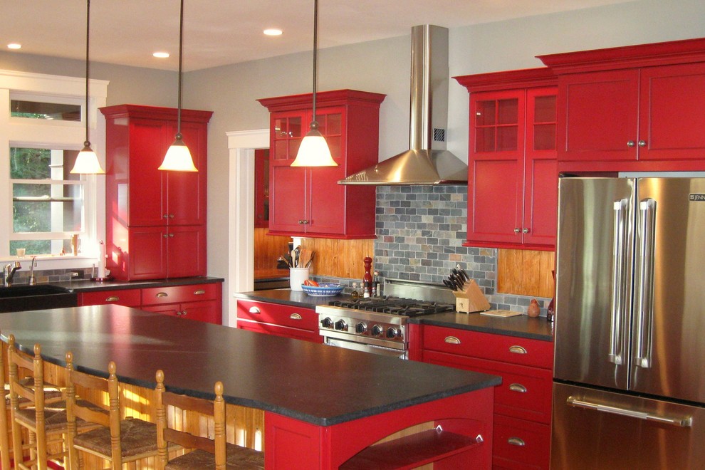 Medium sized contemporary l-shaped kitchen/diner in Boston with a belfast sink, shaker cabinets, red cabinets, soapstone worktops, grey splashback, stone tiled splashback, stainless steel appliances and an island.