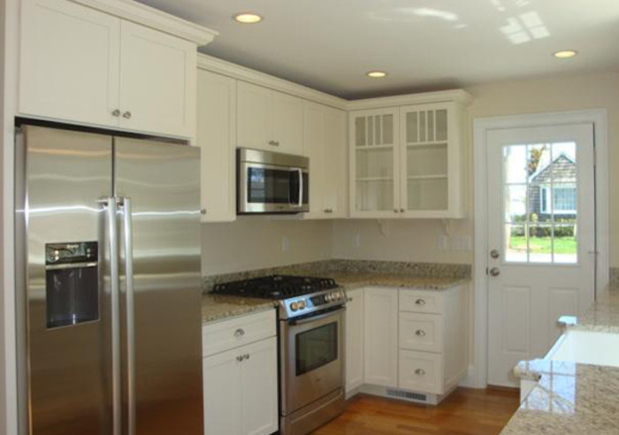Foto på ett litet kök, med luckor med upphöjd panel, vita skåp, granitbänkskiva, rostfria vitvaror och mellanmörkt trägolv