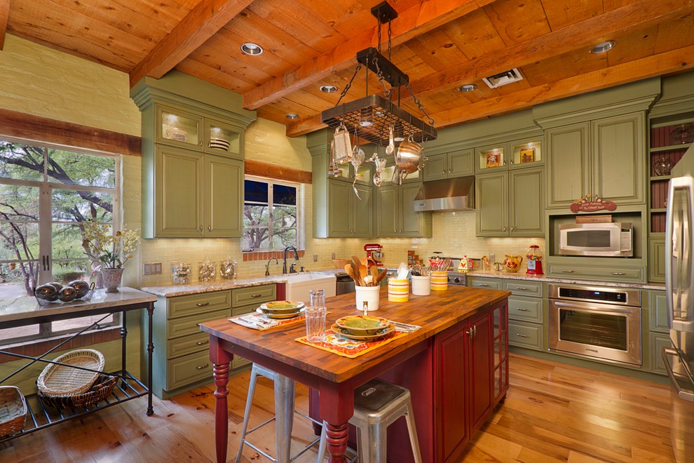 Exempel på ett lantligt u-kök, med luckor med upphöjd panel, gröna skåp, grönt stänkskydd, stänkskydd i glaskakel, rostfria vitvaror, mellanmörkt trägolv och en köksö