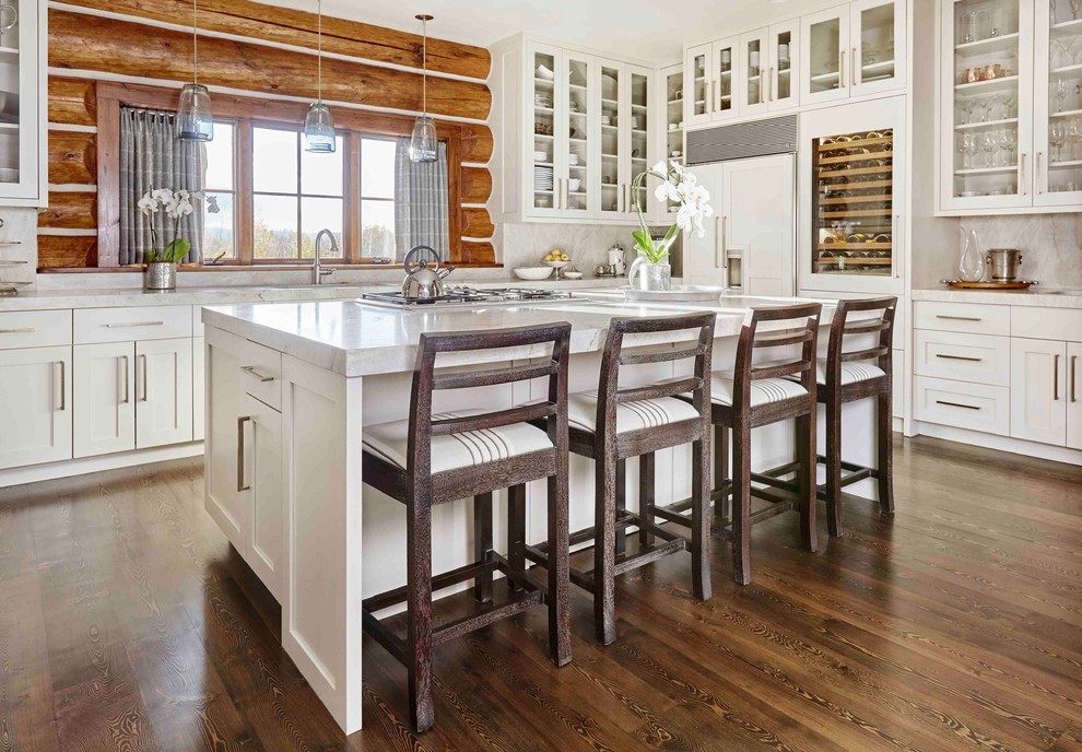 Rustikale Küche in L-Form mit Glasfronten, weißen Schränken, Rückwand-Fenster, Elektrogeräten mit Frontblende, braunem Holzboden, Kücheninsel und braunem Boden in Sonstige