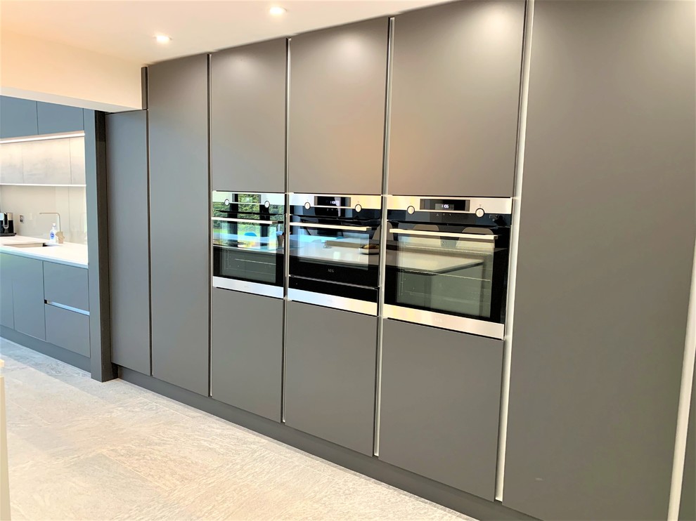 Idee per una grande cucina design con lavello a vasca singola, ante lisce, paraspruzzi con lastra di vetro, elettrodomestici neri e top bianco