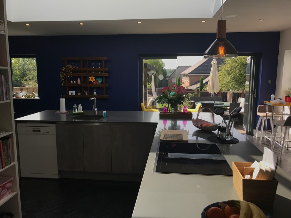 Photo of a large contemporary l-shaped kitchen/diner in Kent with a submerged sink, flat-panel cabinets, white cabinets, quartz worktops, multi-coloured splashback, cement tile splashback, black appliances, vinyl flooring, an island, black floors and grey worktops.
