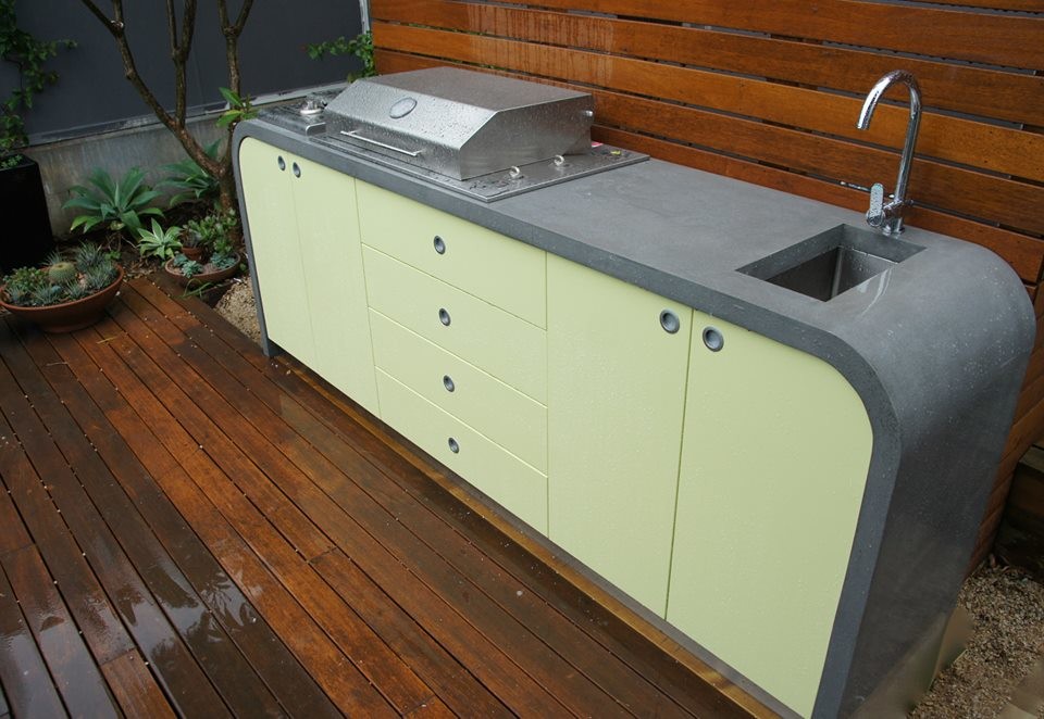 Cette image montre une petite cuisine américaine linéaire minimaliste avec un évier 1 bac, un plan de travail en béton, un électroménager en acier inoxydable, un sol en bois brun et îlot.