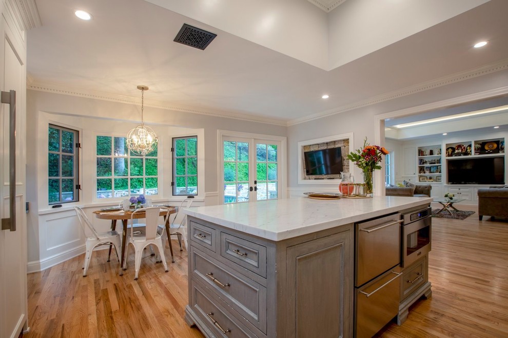 Large transitional u-shaped medium tone wood floor and brown floor eat-in kitchen photo in San Francisco with an undermount sink, recessed-panel cabinets, white cabinets, marble countertops, white backsplash, stone tile backsplash, stainless steel appliances, an island and white countertops