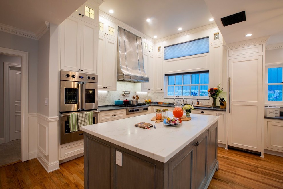 Exempel på ett stort klassiskt vit vitt kök, med en undermonterad diskho, luckor med infälld panel, vita skåp, marmorbänkskiva, vitt stänkskydd, stänkskydd i stenkakel, rostfria vitvaror, mellanmörkt trägolv, en köksö och brunt golv