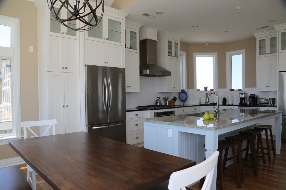 Maritim inredning av ett kök och matrum, med en undermonterad diskho, granitbänkskiva, vitt stänkskydd, stänkskydd i porslinskakel, rostfria vitvaror, mellanmörkt trägolv och en köksö