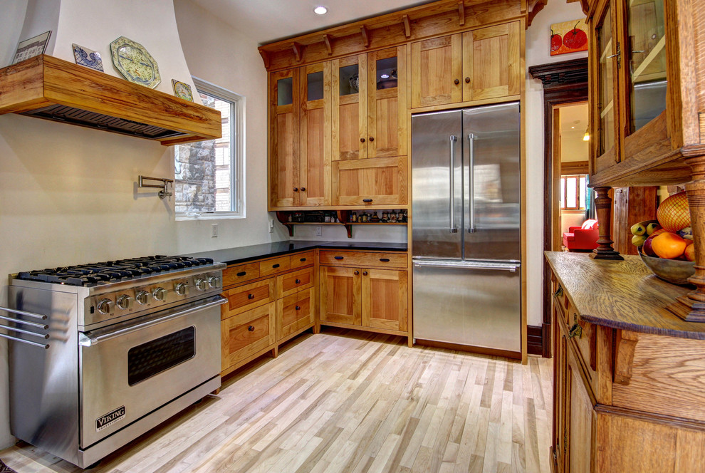 Design ideas for a traditional l-shaped kitchen/diner in Montreal with a belfast sink, shaker cabinets, medium wood cabinets, granite worktops, stainless steel appliances, light hardwood flooring and brown floors.