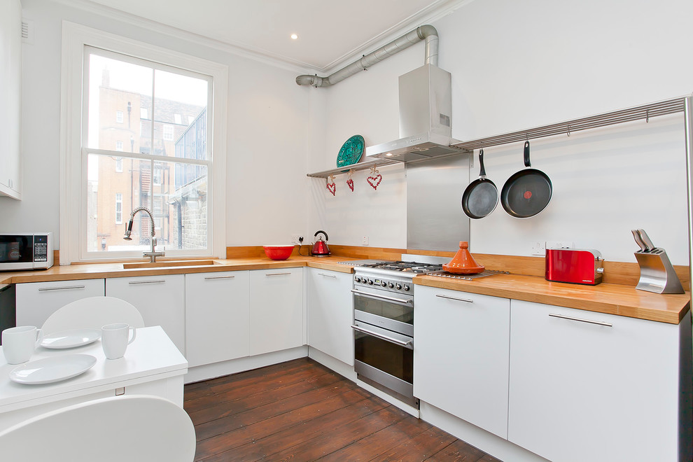 Enclosed kitchen - mid-sized contemporary u-shaped medium tone wood floor enclosed kitchen idea in London with an undermount sink, flat-panel cabinets, white cabinets, wood countertops, white backsplash and no island