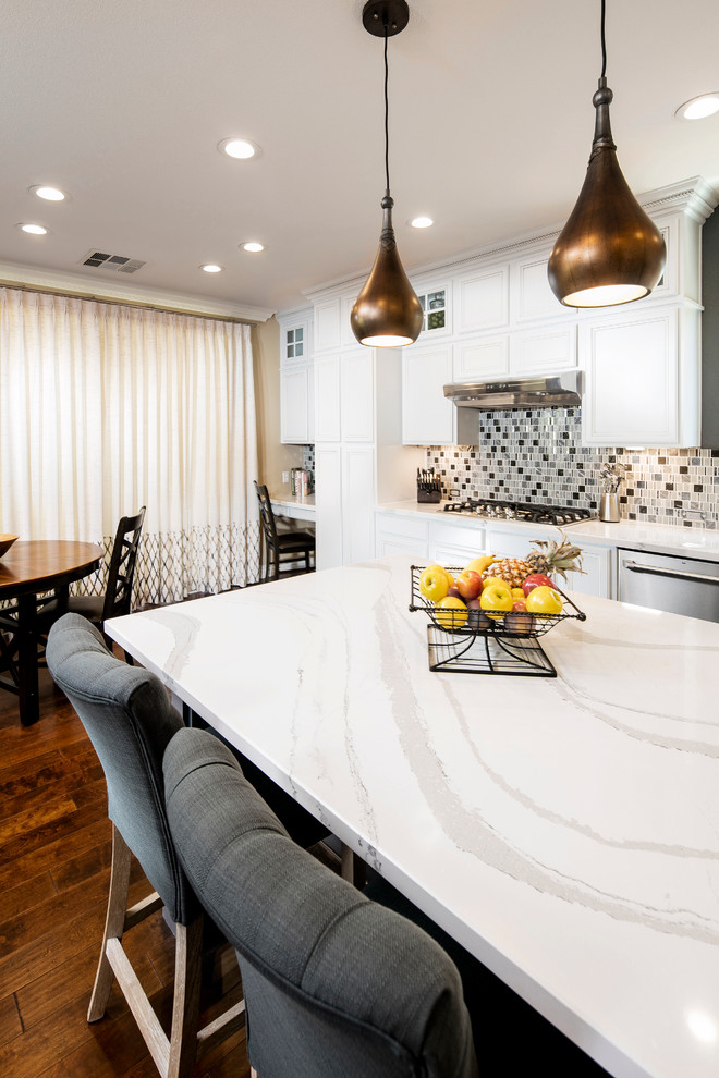 Mid-sized transitional l-shaped medium tone wood floor open concept kitchen photo in Las Vegas with an undermount sink, recessed-panel cabinets, white cabinets, quartz countertops, gray backsplash, glass tile backsplash, stainless steel appliances and an island