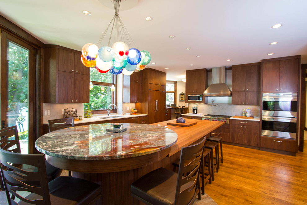 Example of a trendy l-shaped eat-in kitchen design in Minneapolis with an undermount sink, medium tone wood cabinets, granite countertops, gray backsplash, subway tile backsplash, stainless steel appliances and flat-panel cabinets