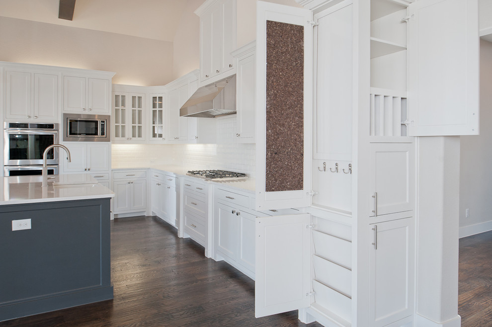 Inspiration for a large transitional l-shaped dark wood floor open concept kitchen remodel in Dallas with a farmhouse sink, shaker cabinets, white cabinets, granite countertops, white backsplash, subway tile backsplash, stainless steel appliances and an island