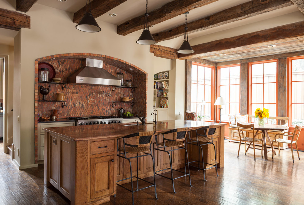 На фото: параллельная кухня в средиземноморском стиле с обеденным столом, фасадами с утопленной филенкой, фасадами цвета дерева среднего тона, красным фартуком и техникой из нержавеющей стали