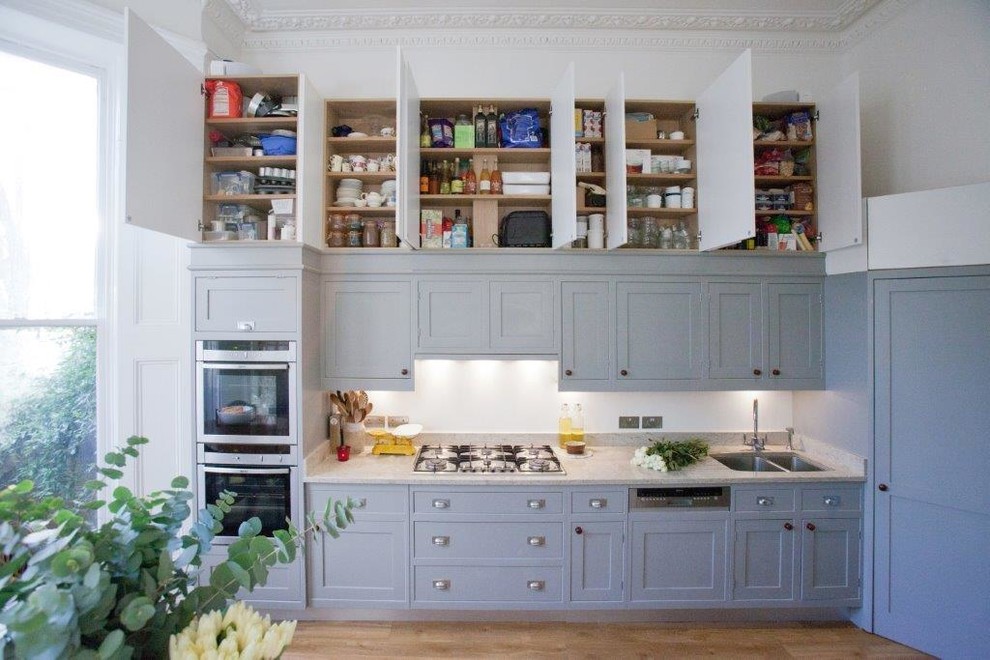 Medium sized classic galley kitchen in London with a double-bowl sink, shaker cabinets, blue cabinets, white splashback, stainless steel appliances, light hardwood flooring and an island.