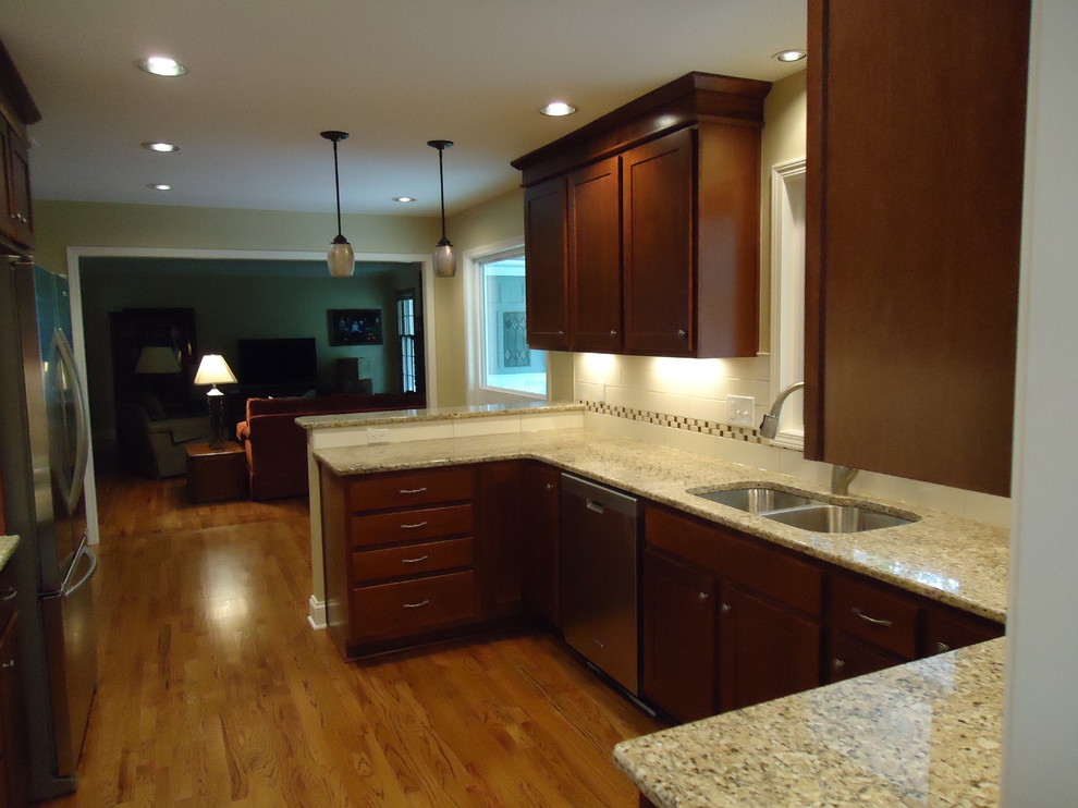 Inspiration for a mid-sized transitional u-shaped dark wood floor and brown floor enclosed kitchen remodel in Kansas City with an undermount sink, dark wood cabinets, granite countertops, white backsplash, ceramic backsplash, stainless steel appliances, shaker cabinets and a peninsula