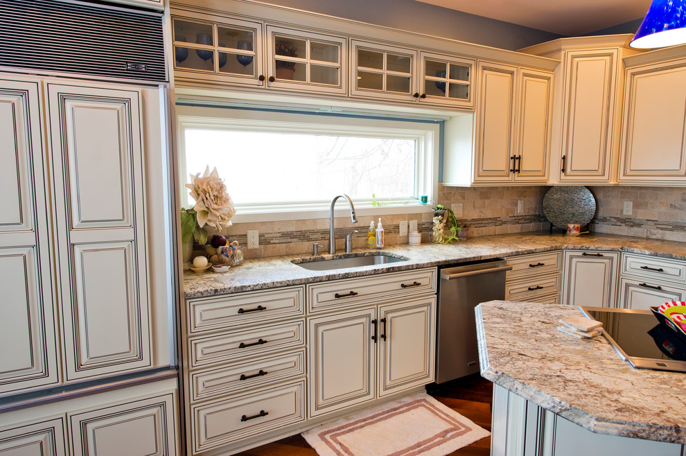 Klassisk inredning av ett mycket stort kök, med en undermonterad diskho, luckor med infälld panel, beige skåp, granitbänkskiva, beige stänkskydd, stänkskydd i stenkakel, rostfria vitvaror, mellanmörkt trägolv och en köksö