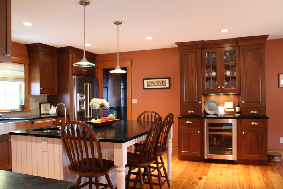 Geschlossene Klassische Küche in L-Form mit Landhausspüle, profilierten Schrankfronten, dunklen Holzschränken, Granit-Arbeitsplatte, Küchenrückwand in Beige, Rückwand aus Steinfliesen, Küchengeräten aus Edelstahl, hellem Holzboden und Kücheninsel in Boston