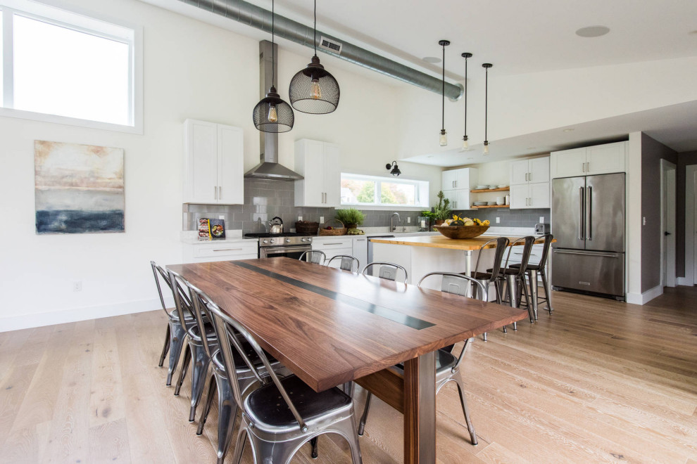 Inspiration for a medium sized urban l-shaped kitchen/diner in Portland Maine with a submerged sink, shaker cabinets, white cabinets, engineered stone countertops, grey splashback, glass tiled splashback, stainless steel appliances, light hardwood flooring, an island, brown floors and white worktops.