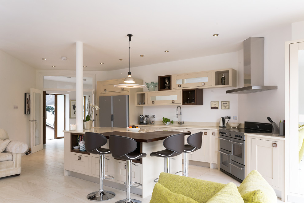 Photo of a large contemporary l-shaped kitchen in Sussex with a submerged sink, shaker cabinets, beige cabinets, white splashback, stainless steel appliances, light hardwood flooring and an island.