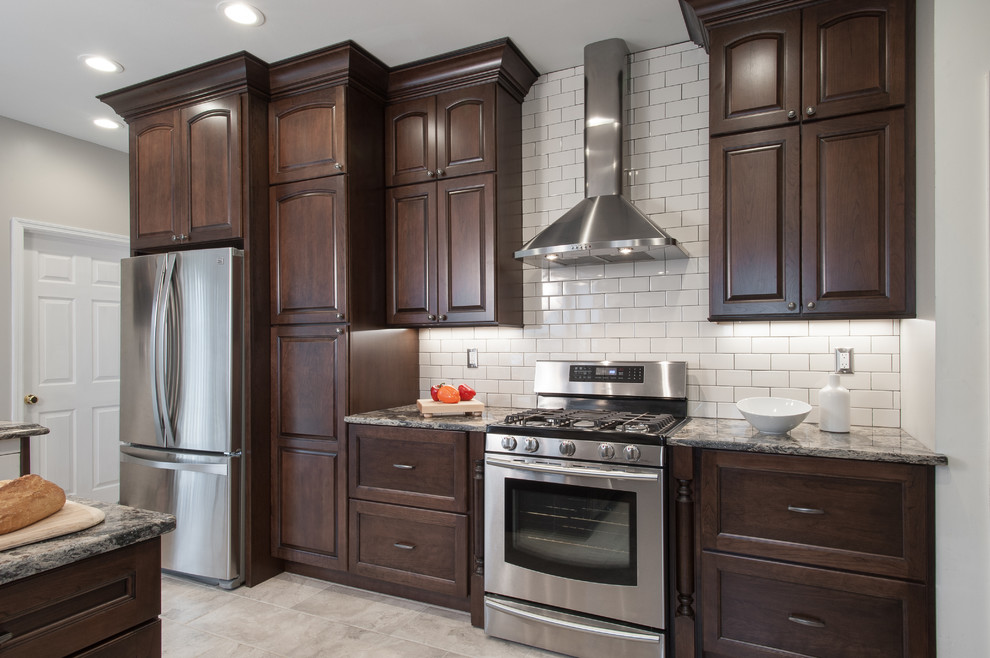 Inspiration for a mid-sized timeless u-shaped ceramic tile eat-in kitchen remodel in St Louis with a farmhouse sink, raised-panel cabinets, dark wood cabinets, granite countertops, white backsplash, subway tile backsplash, stainless steel appliances and a peninsula