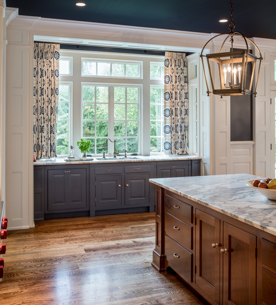 Klassisk inredning av ett mycket stort grå grått kök, med en undermonterad diskho, mellanmörkt trägolv, en köksö, brunt golv, luckor med infälld panel och blå skåp