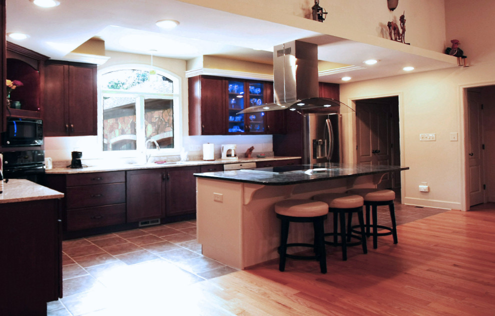 Inredning av ett klassiskt mellanstort svart svart u-kök, med en undermonterad diskho, luckor med infälld panel, skåp i mörkt trä, granitbänkskiva, rostfria vitvaror, en köksö och brunt golv