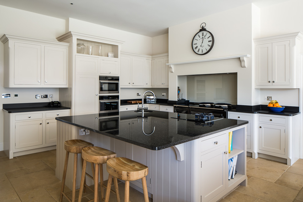 Photo of a large traditional l-shaped kitchen/diner in Other with recessed-panel cabinets, white cabinets, granite worktops, glass sheet splashback, black appliances, an island, beige floors, black worktops, a submerged sink and beige splashback.