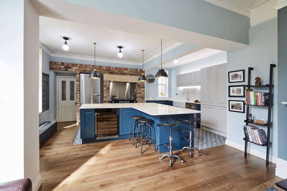This is an example of a medium sized l-shaped kitchen/diner in Other with a belfast sink, shaker cabinets, blue cabinets, marble worktops, white splashback, marble splashback, stainless steel appliances, porcelain flooring, multiple islands, blue floors, white worktops and a coffered ceiling.