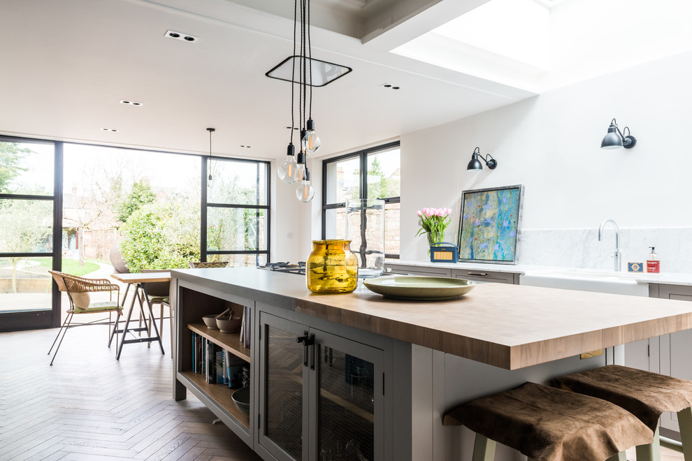 Large contemporary u-shaped kitchen/diner in London with a submerged sink, flat-panel cabinets, grey cabinets, composite countertops, white splashback, marble splashback, stainless steel appliances, light hardwood flooring and an island.