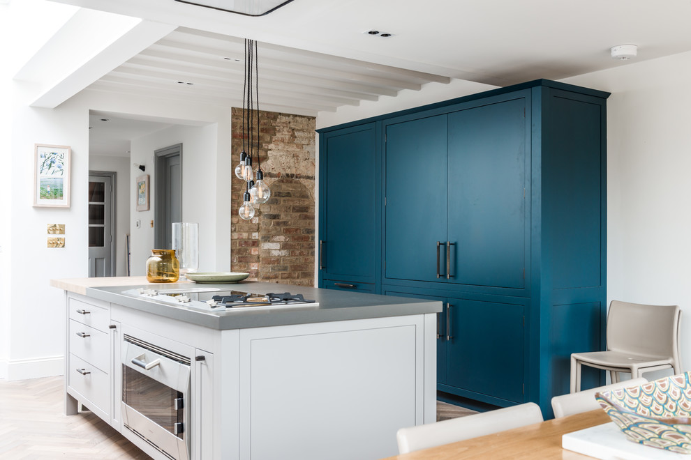 Design ideas for a large contemporary u-shaped kitchen/diner in London with a submerged sink, flat-panel cabinets, composite countertops, white splashback, marble splashback, stainless steel appliances, light hardwood flooring, an island and blue cabinets.