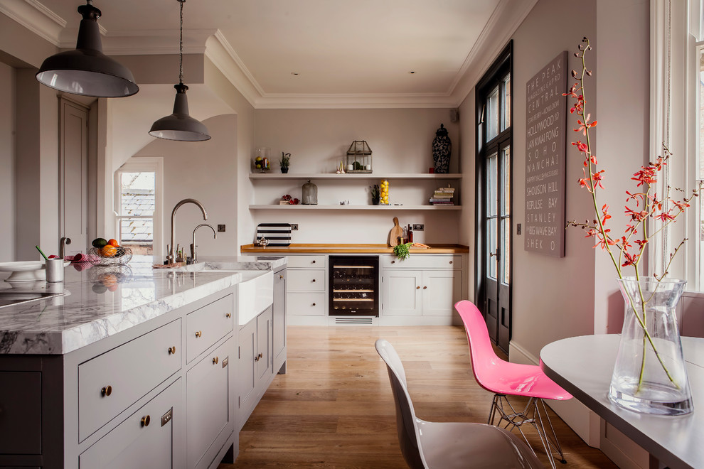 Klassische Wohnküche mit Landhausspüle, Schrankfronten im Shaker-Stil, grauen Schränken, Marmor-Arbeitsplatte, braunem Holzboden und Kücheninsel in Hampshire