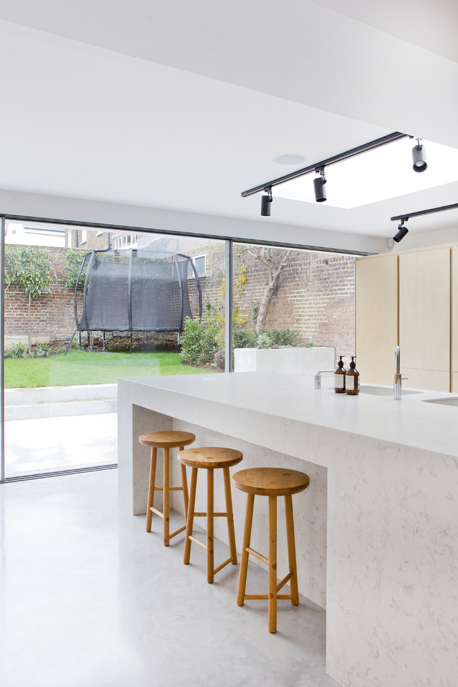 Example of a minimalist kitchen design in London with white backsplash, an island and white countertops
