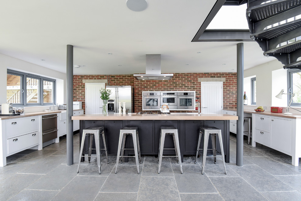 Inspiration for a traditional u-shaped kitchen in Other with flat-panel cabinets, white cabinets, wood worktops, stainless steel appliances, an island, grey floors and beige worktops.