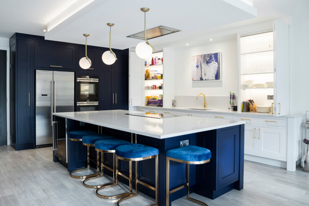 Große Klassische Küche in L-Form mit Unterbauwaschbecken, Schrankfronten im Shaker-Stil, blauen Schränken, Küchenrückwand in Grau, Küchengeräten aus Edelstahl, Kücheninsel, grauem Boden und weißer Arbeitsplatte in Sonstige