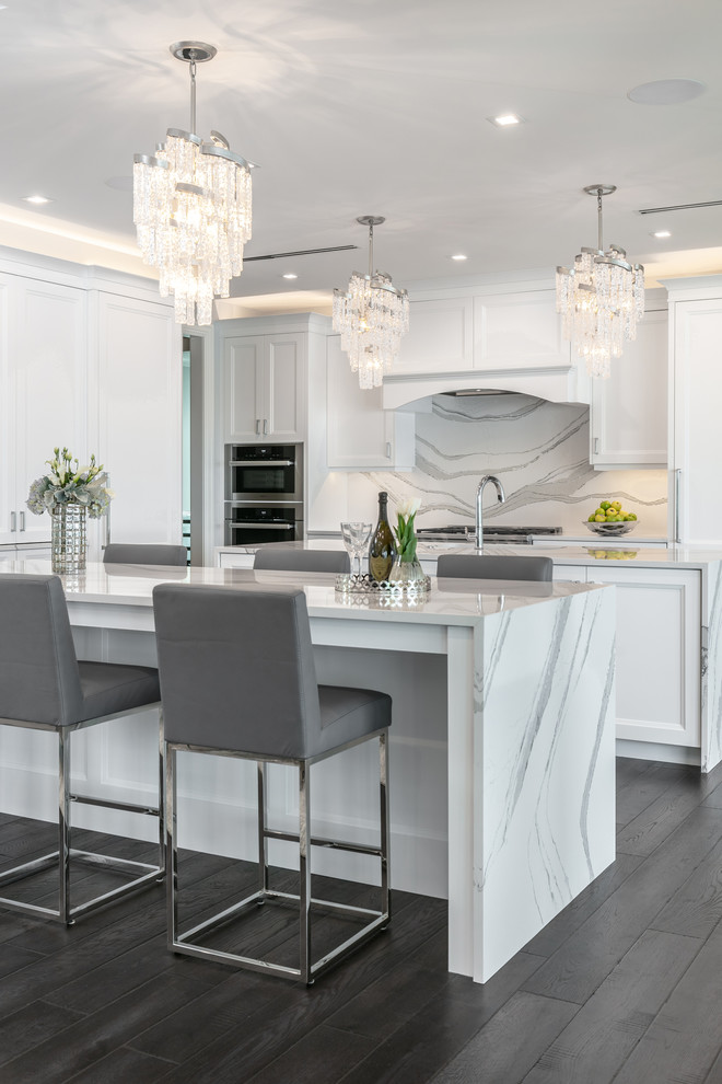Moderne Wohnküche in L-Form mit Schrankfronten mit vertiefter Füllung, weißen Schränken, Küchenrückwand in Weiß, Küchengeräten aus Edelstahl, Kücheninsel, weißer Arbeitsplatte, braunem Holzboden und grauem Boden in Tampa