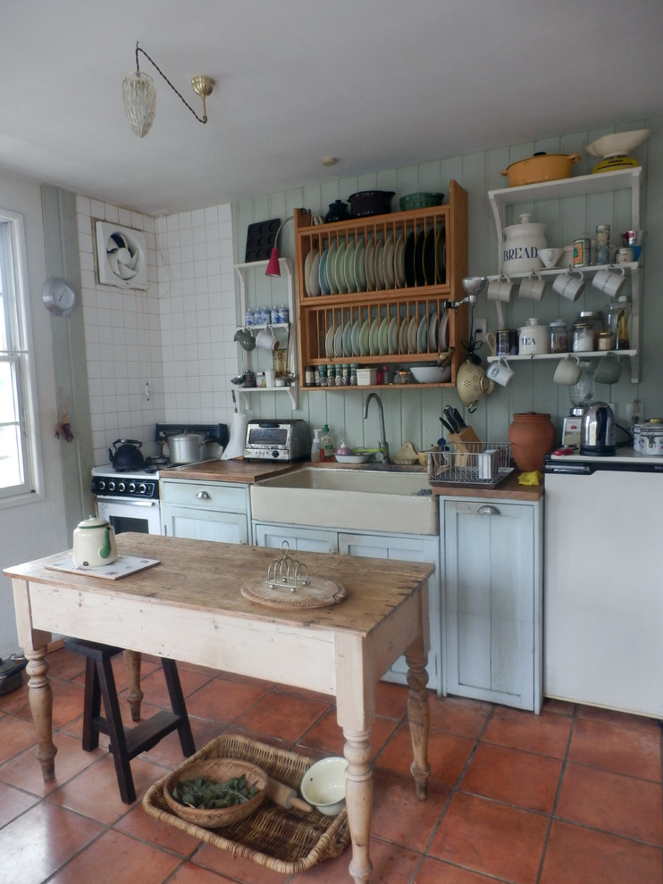 На фото: прямая кухня с обеденным столом, одинарной мойкой, синими фасадами, деревянной столешницей, зеленым фартуком, полом из терракотовой плитки и островом с