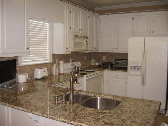 На фото: угловая кухня в классическом стиле с белыми фасадами, гранитной столешницей, белой техникой и полуостровом