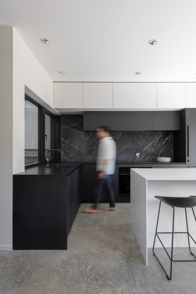 This is an example of a large contemporary l-shaped kitchen in Vancouver with a submerged sink, flat-panel cabinets, black cabinets, black splashback, porcelain splashback, integrated appliances, an island, grey floors and black worktops.