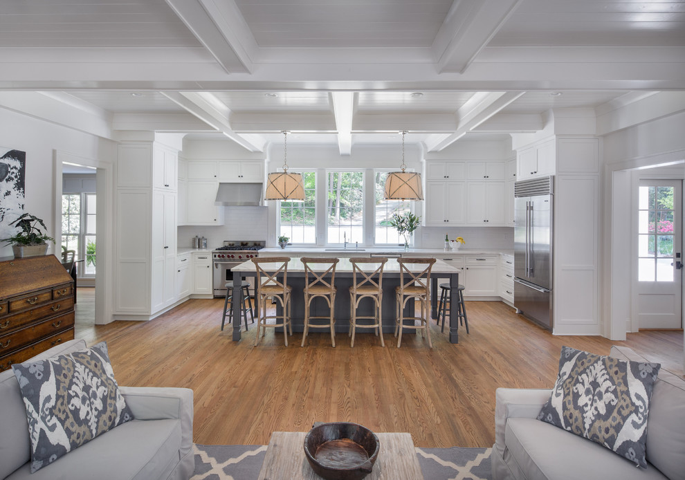 Mid-sized transitional l-shaped medium tone wood floor and brown floor kitchen photo in Atlanta with an undermount sink, shaker cabinets, white cabinets, marble countertops, white backsplash, ceramic backsplash, stainless steel appliances and an island