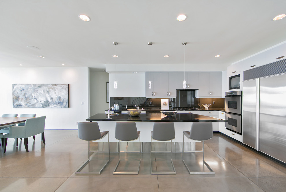 Contemporary l-shaped kitchen in Orange County with a submerged sink, flat-panel cabinets, grey cabinets, black splashback, glass sheet splashback, stainless steel appliances, concrete flooring, an island and grey floors.