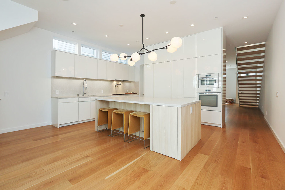 Exemple d'une cuisine tendance en L avec un placard à porte plane, des portes de placard blanches, une crédence grise, un sol en bois brun et îlot.