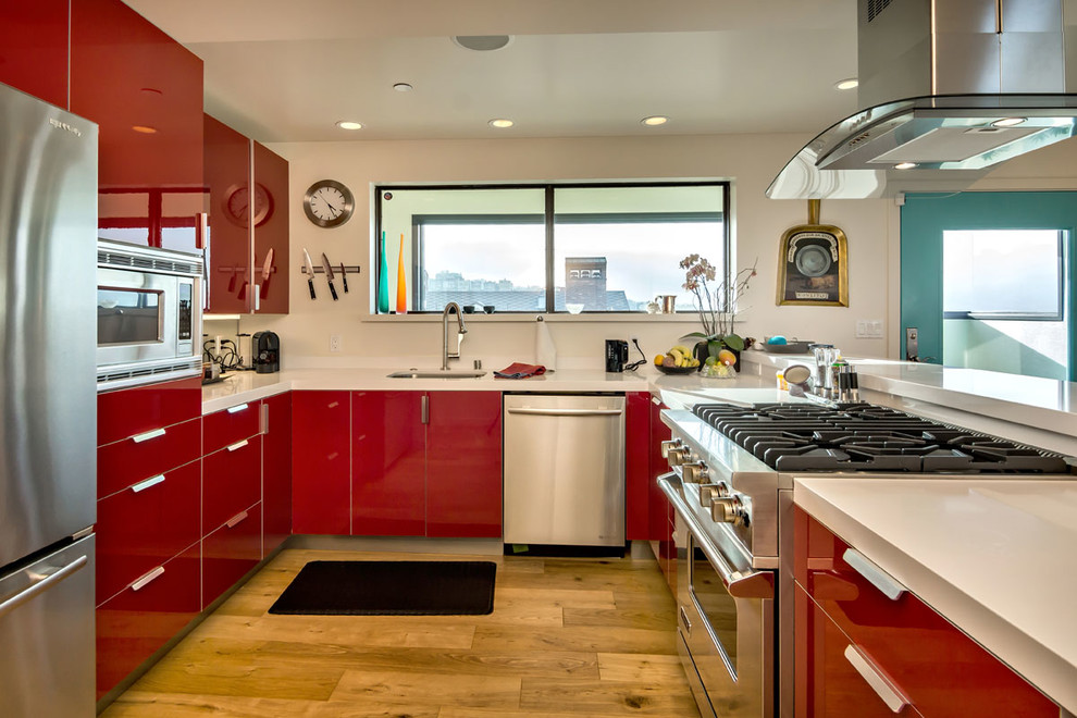 На фото: п-образная кухня-гостиная в современном стиле с врезной мойкой, плоскими фасадами, красными фасадами и техникой из нержавеющей стали с