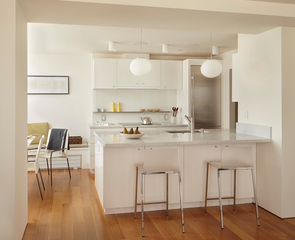 This is an example of a contemporary galley kitchen/diner in San Francisco with flat-panel cabinets, white cabinets, white splashback, glass sheet splashback, stainless steel appliances, medium hardwood flooring and a breakfast bar.