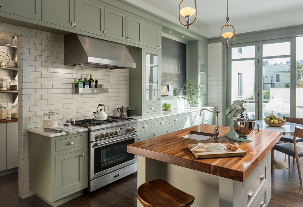 Exempel på ett klassiskt kök, med en undermonterad diskho, skåp i shakerstil, gröna skåp, träbänkskiva, vitt stänkskydd, stänkskydd i tunnelbanekakel, rostfria vitvaror, mörkt trägolv och en köksö