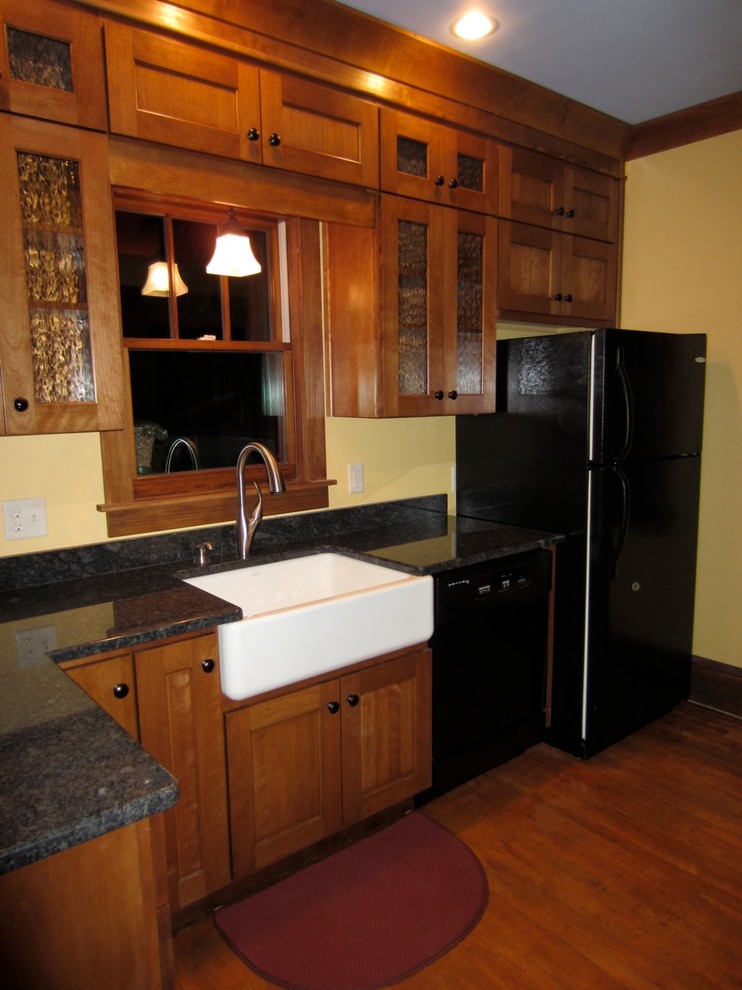 Cette photo montre une cuisine parallèle craftsman en bois brun fermée avec un évier de ferme, un placard à porte shaker, un plan de travail en granite et un électroménager noir.